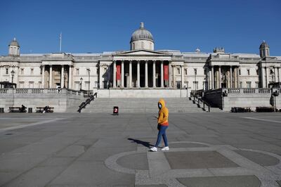 A masked visitor walks past the National Gallery in a near deserted Trafalgar Square in central London on March 25, 2020, after Britain's government ordered a lockdown to slow the spread of the novel coronavirus. Britain was under lockdown, its population joining around 1.7 billion people around the globe ordered to stay indoors to curb the "accelerating" spread of the coronavirus. / AFP / Tolga AKMEN
