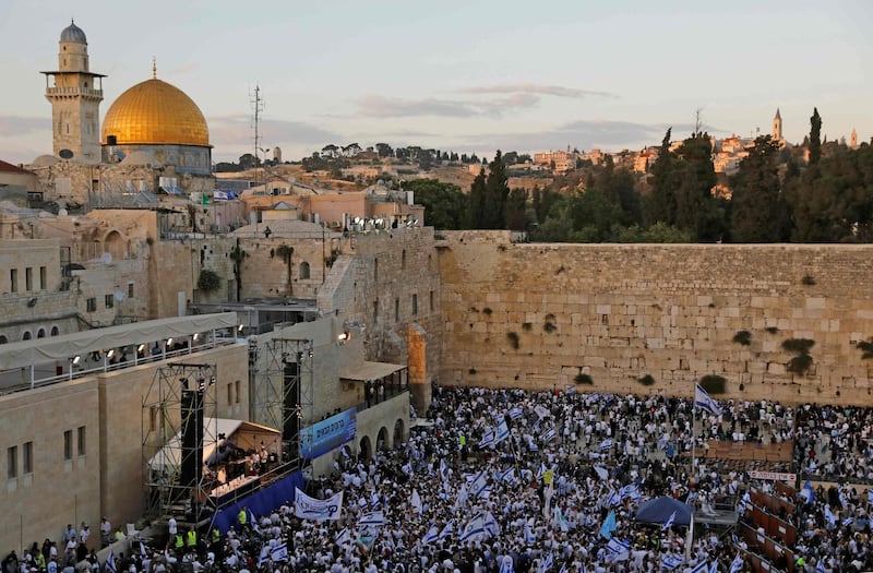 Isreali nationalist settlers wave their national flags in front of the Western Wall in Jerusalem's Old City on May 13, 2018, as they celebrate the Jerusalem Day with the dome of the Rock in the background. For Israelis, Sunday is Jerusalem Day, an annual celebration of the "reunification" of the city following the 1967 Six-Day War. / AFP / MENAHEM KAHANA
