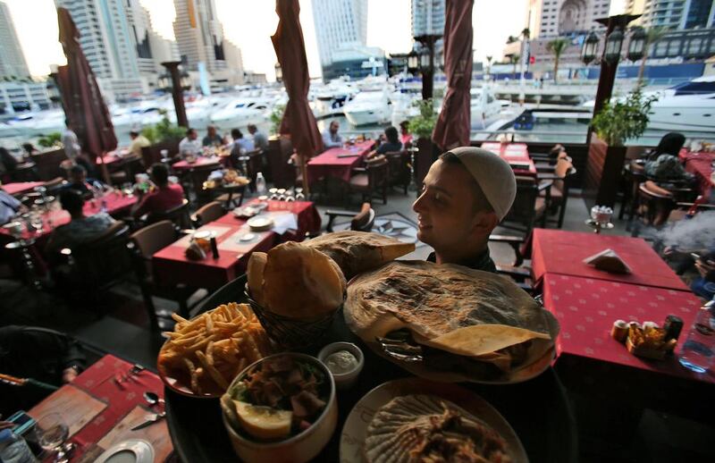 A waiter carries a tray of Arabic food at a restaurant in Dubai Marina. The emirate is now home to more than 16,000 food outlets Kamran Jebreili / AP Photo