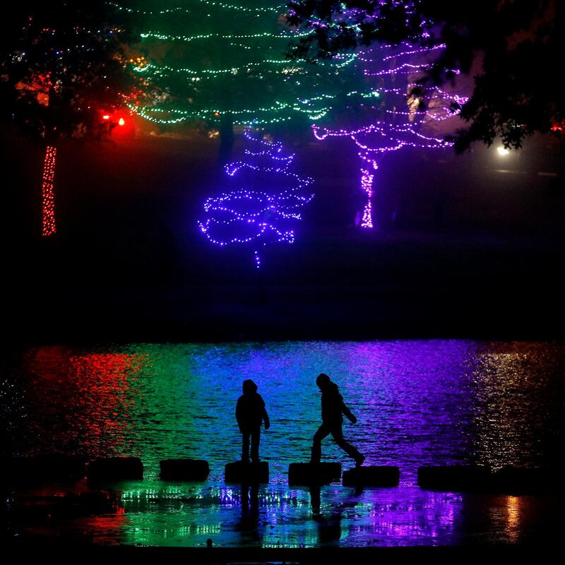 Children are silhouetted against holiday lights reflecting off a pond in a park. AP