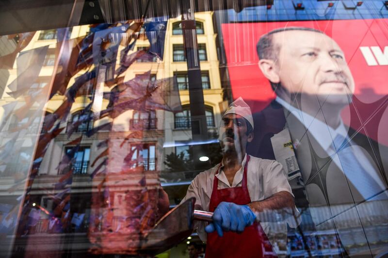 A kebab shop worker slices meat as the reflection of Turkish president Recep Tayyip Erdogan is seen on the window of a restaurant in Taksim Square, Istanbul. Bulent Kilic / AFP Photo