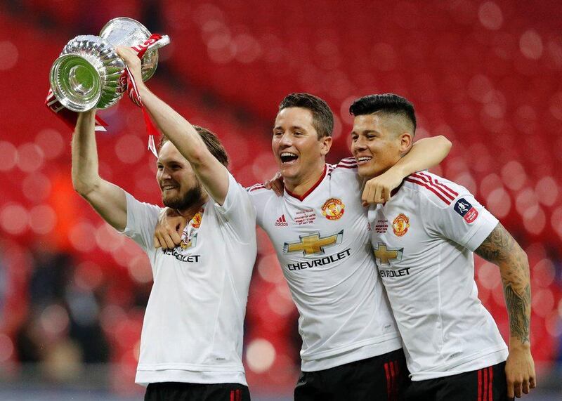 Manchester United’s Dutch midfielder Daley Blind (L) holds up the trophy as he celebrates on the pitch with Manchester United’s Spanish midfielder Ander Herrera (C) and Manchester United’s Argentinian defender Marcos Rojo (R) after their victory after extra time in the English FA Cup final football match between Crystal Palace and Manchester United at Wembley stadium in London on May 21, 2016. Manchester United won the game 2-1, after extra time. Adrian Dennis / AFP