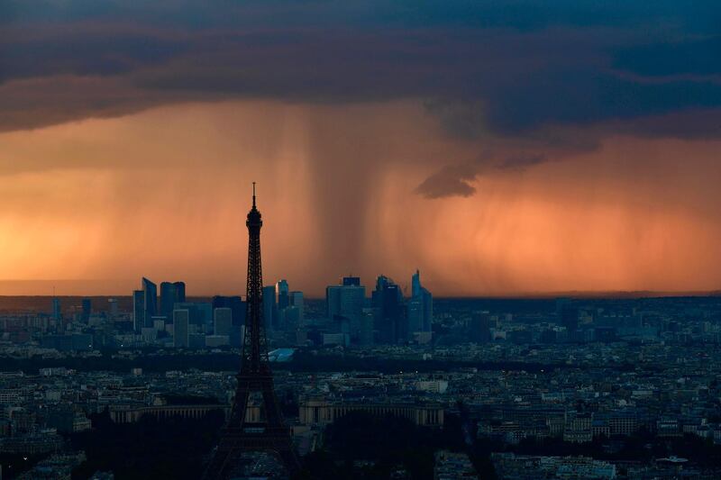 A picture taken from the observatory deck of the Montparnasse tower in Paris shows the Eiffel Tower in Paris and La Defense business district under heavy clouds at sunset.  Philippe Lopez / AFP