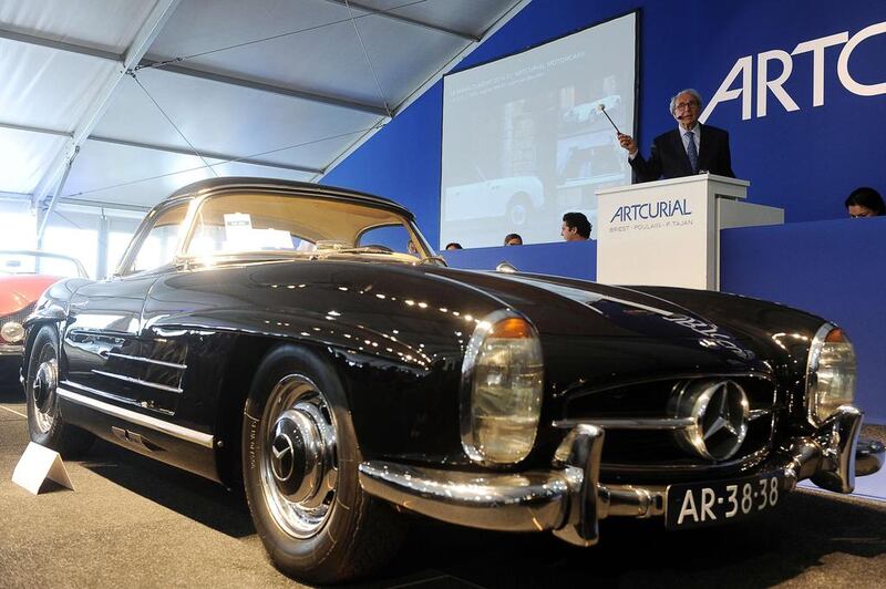 French auctioneer and former racing driver Herve Poulain gestures behind a 1961 Mercedes-Benz 300 SL Roadster Hard Top during a classic car auction in Le Mans, western France, on July 5, 2014. The car was sold for 1,115,600 euros (Dh5,570,547) at an auction held during the Le Mans Classic event, breaking the record for a vintage car auction, Artcurial, which organized the auction, announced on July 5. The auction of a hundred racing cars, organized by “Artcurial Motorcars” takes place during the Le Mans Classic race, which takes place every two years on the Le Mans circuit. AFP 