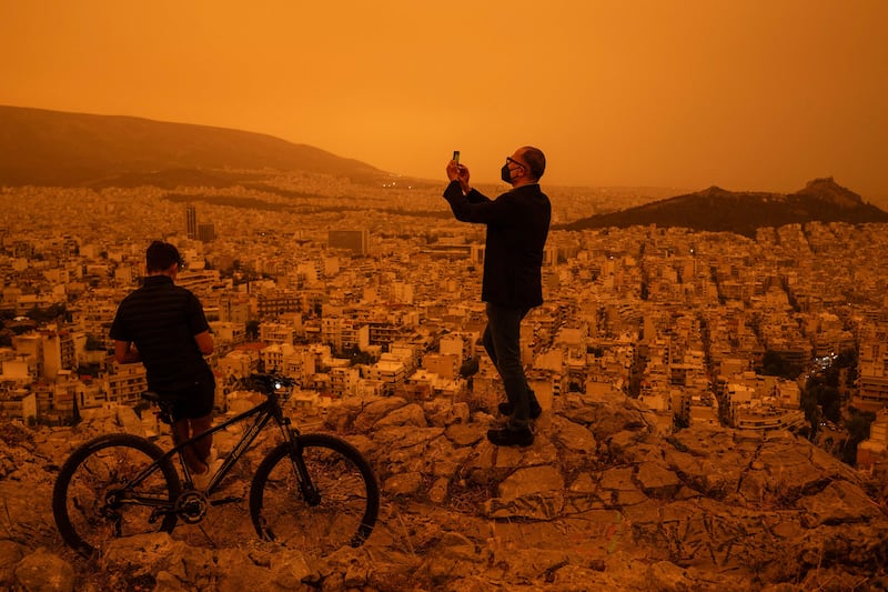 A man takes a photograph of the city of Athens from Tourkovounia hill.  The yellow-orange haze smothered several regions, limiting visibility and prompting warnings of breathing risks from the authorities. AFP