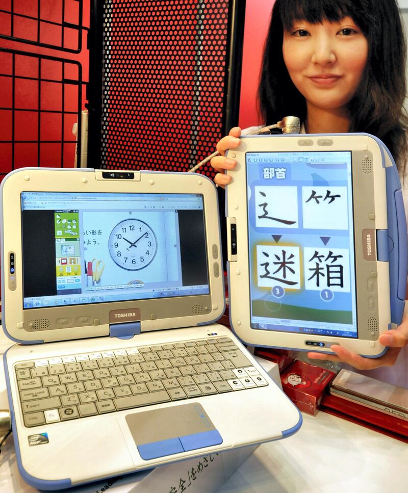 An employee of Japanese electronics company Toshiba displays their new CM1 touch screen tablet PC (R) for educational use that converts into the style of a conventional laptop (L) at the International Book Fair in Tokyo on July 9, 2010. Japanese government has set out a policy of providing digital textbooks for all elementary and junior high school students by 2015. AFP PHOTO/Yoshikazu TSUNO (Photo by YOSHIKAZU TSUNO / AFP)