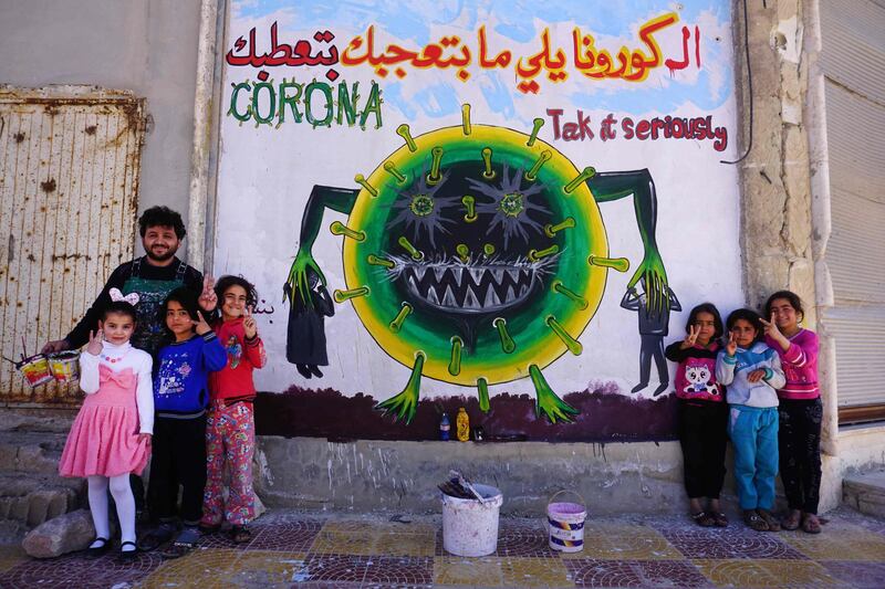 Syrian artist Aziz al-Asmar and children flash the victory gesture as they pose next to freshly-drawn graffiti on the wall of a building in Binnish in Syria's northwestern Idlib province. AFP