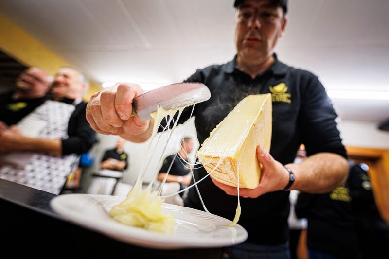 A "scaper" prepares a raclette during the first-ever Raclette World Championships featuring local and international raclette cheeses, in Morgins, on October 28, 2023.  Up in the Swiss Alps, the air hangs thick with the funk of hot cheese as the planet's best melt away the competition at the inaugural Raclette World Championships.  The Swiss native dish dates back centuries to a time when mountain herdsmen would heat their cheese on an open fire and scrape off the melted part to keep them going.  (Photo by VALENTIN FLAURAUD  /  AFP)