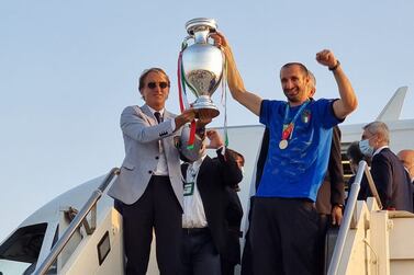 This handout picture taken and released by the Aereoporti Di Roma (A. D. R. ) on July 12, 2021 shows italian coach Roberto Mancini (L) and Giorgio Chiellini holding the European Championship trophy after Italy won the UEFA EURO 2020 final football match between Italy and England, as they arrive at Rome's Fiumicino airport in Rome.  (Photo by - / AEROPORTO DI ROMA / AFP) / RESTRICTED TO EDITORIAL USE - MANDATORY CREDIT "AFP PHOTO /  Aereoporti Di Roma (A. D. R. ) " - NO MARKETING - NO ADVERTISING CAMPAIGNS - DISTRIBUTED AS A SERVICE TO CLIENTS