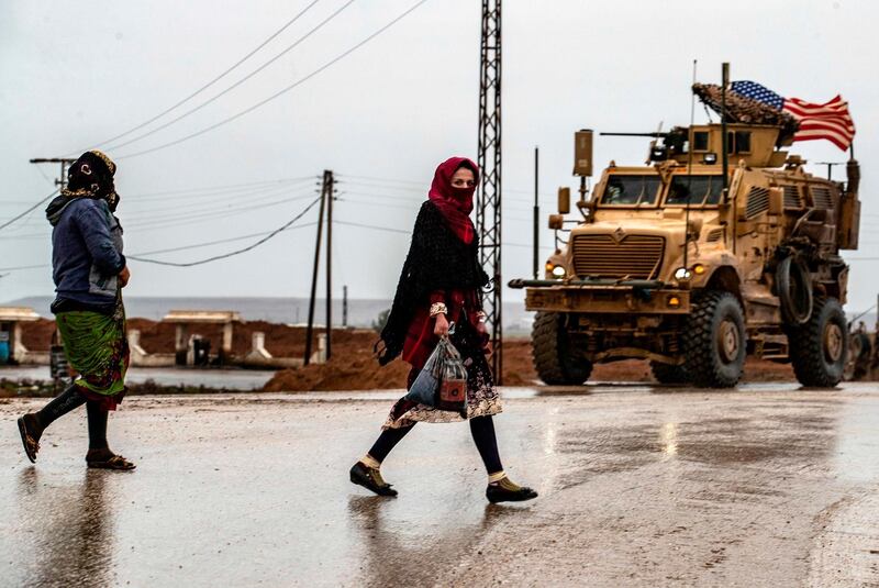Women walk past an American army vehicle on the M4 highway in the town of Tal Tamr in the northeastern Syrian Hasakeh province on the border with Turkey.   AFP