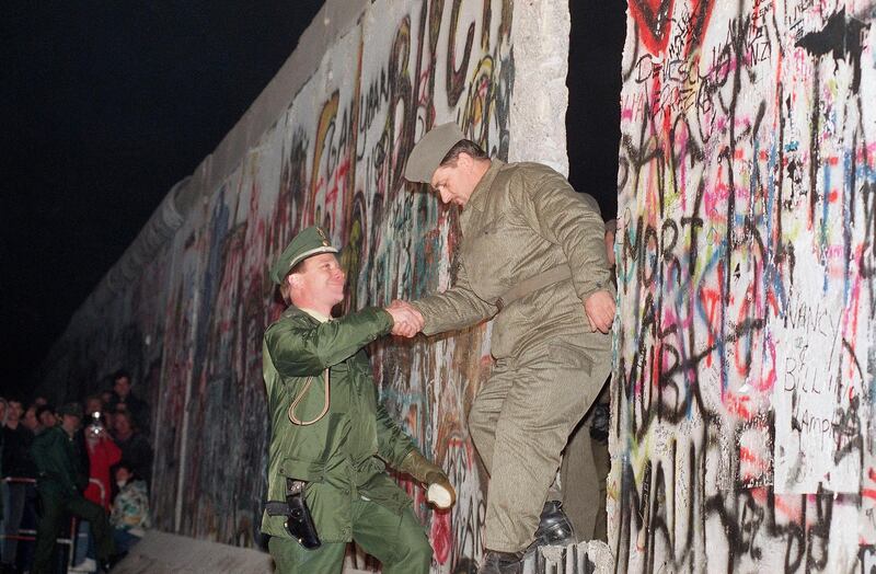 West German policeman, left, gives a helping hand to an East German border guard who climbs through a gap of the Berlin Wall when East Germany opened another passage at Potsdamer Platz in Berlin. AP Photo