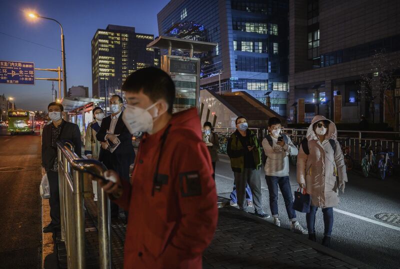 Chinese commuters wear protective masks as they line up in a staggered formation while waiting for a bus at the end of the work day in Beijing. Getty Images