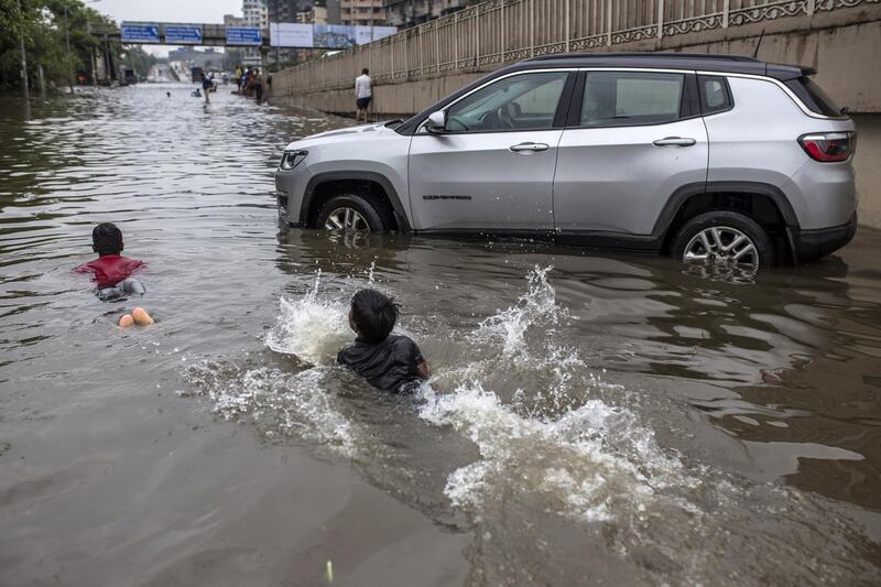 Children swim past an abandoned vehicle in a flooded road in Mumbai, India. Bloomberg