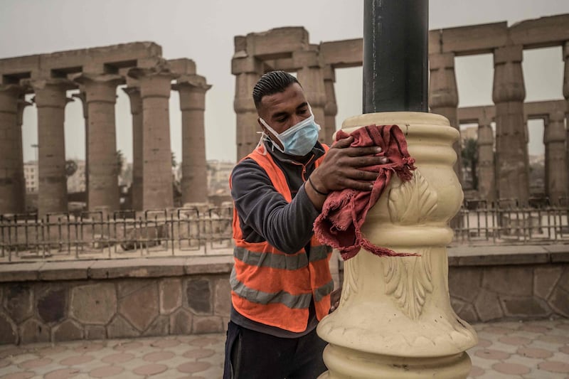 A municipality worker cleans lamp posts amid a sandstorm and coronavirus fears outside the Luxor Temple in Egypt's southern city of Luxor.  AFP