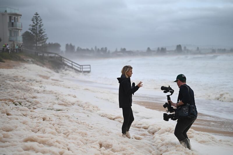 A news team films sea foam brought in by waves after heavy rain and storms at Collaroy in Sydney.  EPA