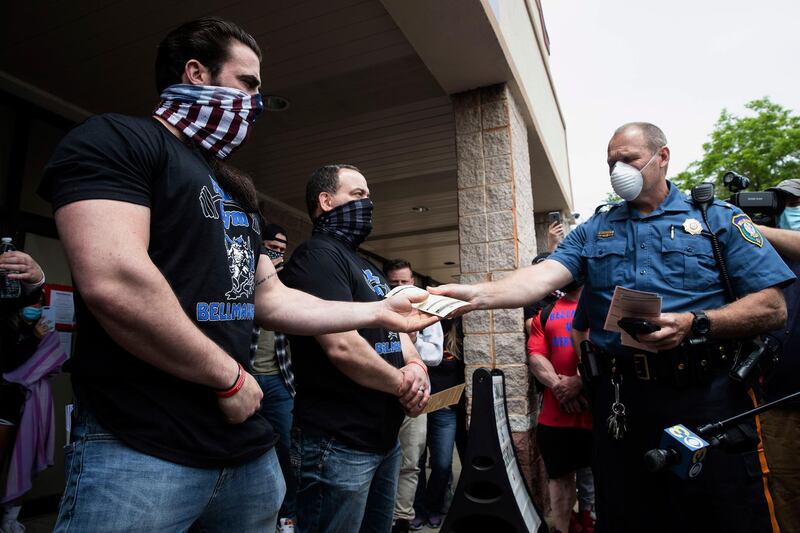 A police officer issues Atilis Gym co-owners Ian Smith, left, and Frank Trumbetti summons outside their gym in Bellmawr, N.J. The New Jersey gym reopened for business early Monday, defying a state order that shut down nonessential businesses to help stem the spread of the coronavirus. AP Photo