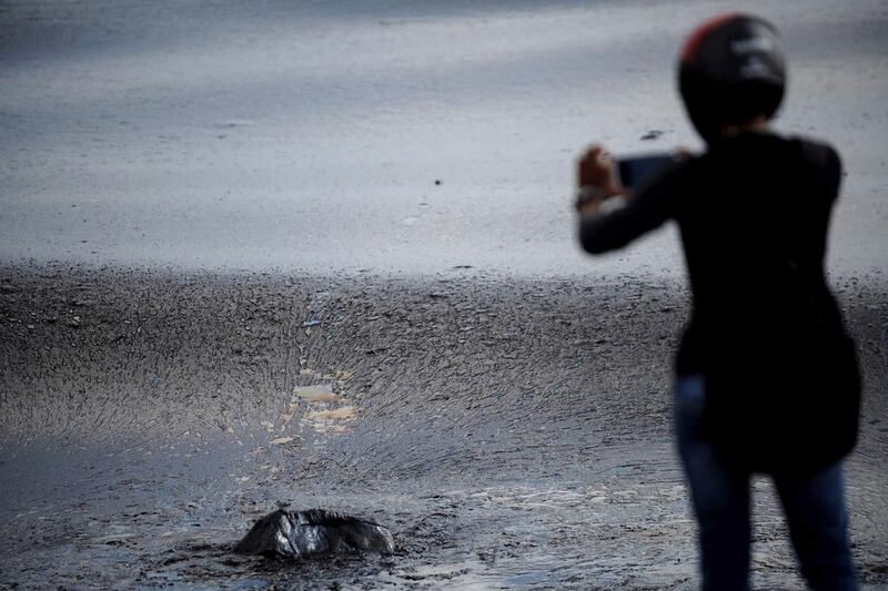A man takes a photograph of black oil as a thick oily tide from the sea laps at the coast, a day after an oil tanker and an LPG tanker collided off Kamarajar Port in Ennore, in Chennai. Arun Sankar / AFP