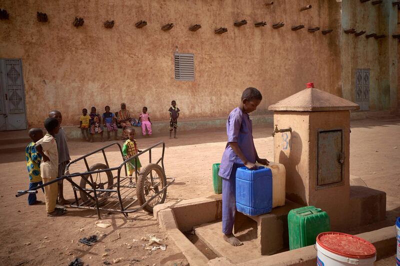 Children fill gallons with water at a pump outside the great mosque in Konna on March 20, 2021 as the Malian Prime Minister and his delegation visit the town in central Mali to attend the inauguration of the new river port, which was destroyed by bombing during the war in 2013. - Located some 50 kilometres north of Mopti, the town of Konna used to be a key area for fishing activities in central Mali. (Photo by MICHELE CATTANI / AFP)