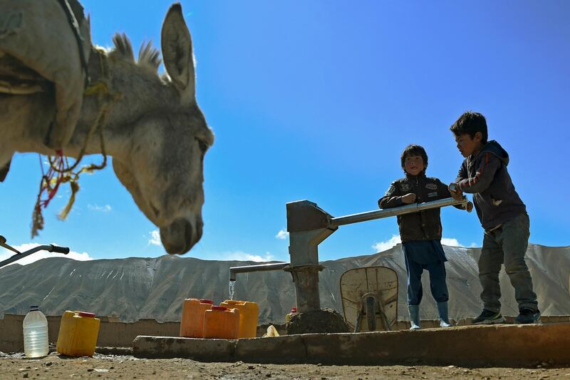 Hazara boys fill water from a hand-pump on the outskirts of Bamiyan province on March 7, 2021. (Photo by WAKIL KOHSAR / AFP)