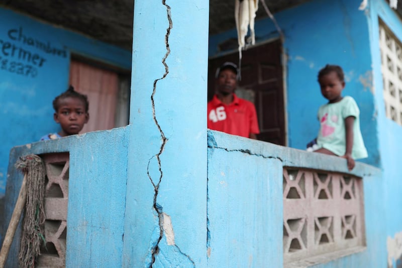 A man and two children stand on the porch of their home after it was damaged in an earthquake in Port-de-Paix, Haiti. Reuters