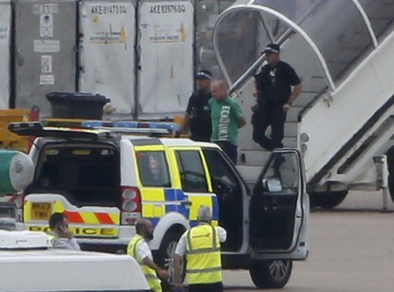 A man in a green T-shirt is escorted off the Qatar Airways plane by police at Manchester airport. Andrew Yates / Reuters