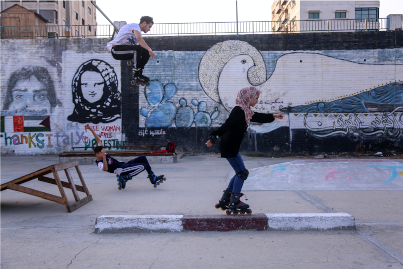 Teens rollerblading on a rooftop in Gaza with murals as a backdrop. Photo by Samar Abu Elouf