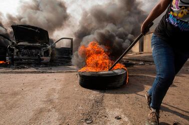 An Iraqi demonstrator moves a burning tyre next to the smoking remains of an Iraqi anti-riot vehicle during a demonstration in the southern city of Basra on Sunday. AFP