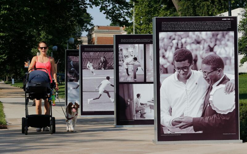 A passerby walks by a row of photographs of tennis star Arthur Ashe in front of the Virginia Museum of History & Culture as part of an exhibit titled Determined The 400-year struggle for Black Equality at the museum in Richmond, Va., Thursday, June 20, 2019. The exhibit is scheduled to open June 22. (AP Photo/Steve Helber)