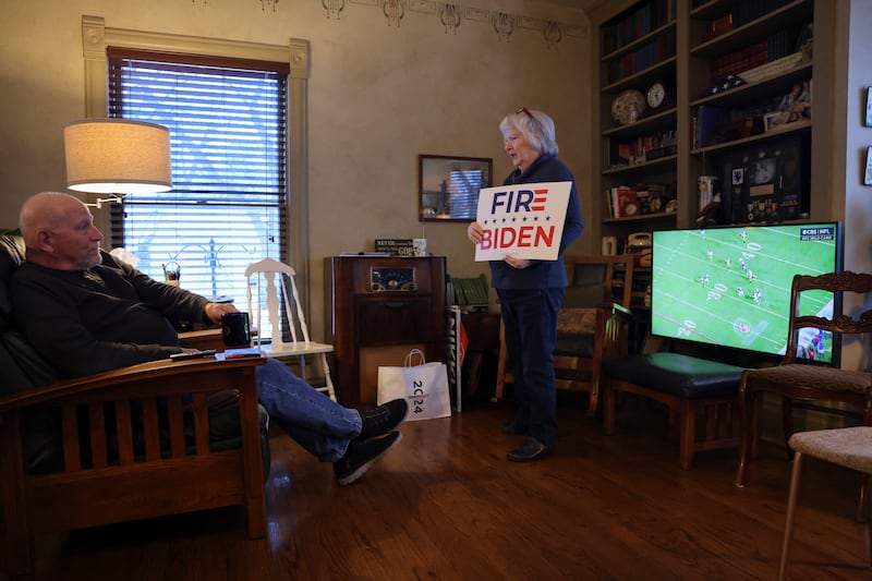 A woman holds a campaign sign  while her husband watches an American football game, as they prepare to hold a caucus at their home in Silver City, Iowa. Reuters