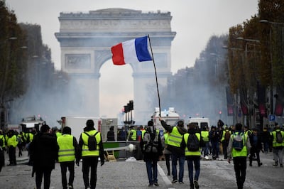 Yellow vest (Gilet jaune) protestors hold a French flag on the Champs Elysees in Paris, on November 24, 2018 during a protest against rising oil prices and living costs. - Police fired tear gas and water cannon on November 24 in central Paris against "yellow vest" protesters demanding French President Emmanuel Macron roll back tax hikes on motor fuel. (Photo by Bertrand GUAY / AFP)