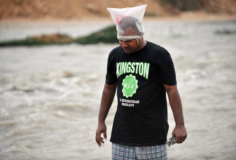 A man in Saudi has a plastic bag on his head to protect himself from the rain as tries to catch fish in the Nimar valley, south of the Saudi capital Riyadh. Fayez Nureldine / AFP Photo

