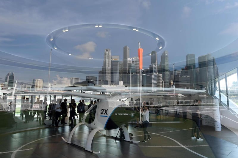 The city skyline with the prototype of Voloport launch pad are reflected on a glass panel while visitors view the Volocopter unmanned air taxi transport displayed ahead of the 26th Intelligent Transport Systems World Congress (ITSWC) in Singapore.  AFP