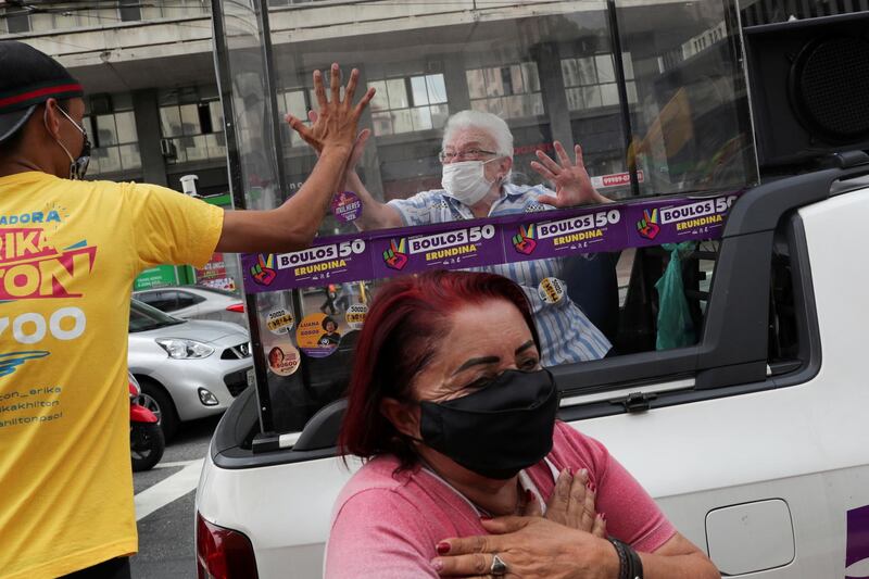 Luiza Erundina, 85, a candidate for vice-mayor, holds her hand to a man's from inside the "cata voto" (Vote Catcher), a car with a plastic booth, in Sao Paulo, Brazil. Reuters