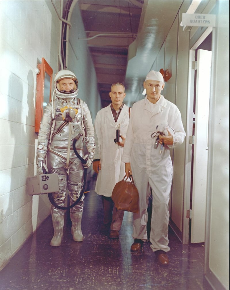 Astronaut John H. Glenn Jr., NASA flight surgeon William Douglas and equipment specialist Joseph W. Schmidt leave crew quarters prior to the Mercury-Atlas 6 mission. Glenn is in his pressure suit and is carrying the portable ventilation unit. Courtesy Nasa