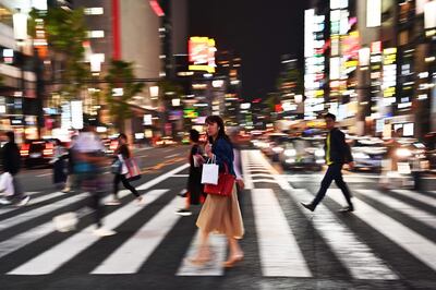 A woman crosses a street at night in Tokyo on April 22, 2019. / AFP / CHARLY TRIBALLEAU
