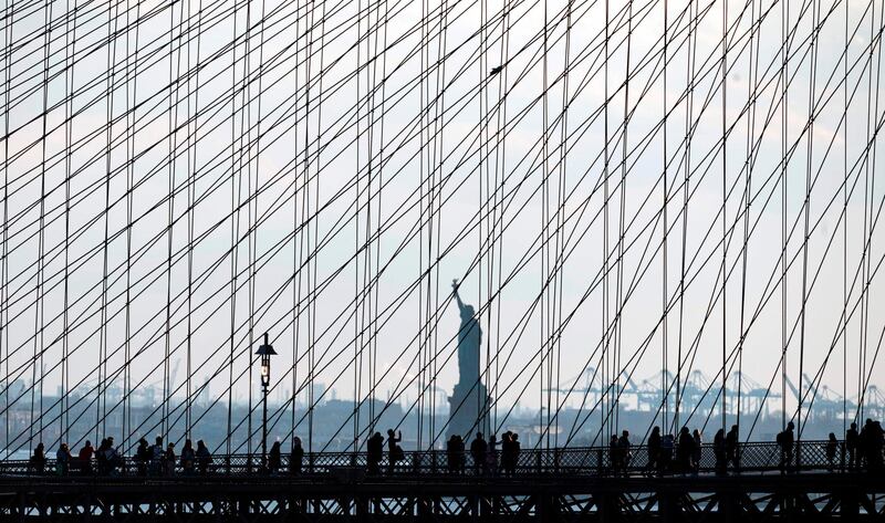 People walk on the Brooklyn Bridge in front of the Statue of Liberty in New York City. AFP