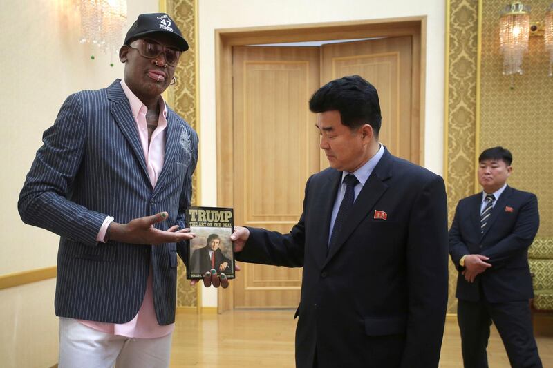 FILE - In this June 15, 2017, file photo, former NBA basketball star Dennis Rodman presents a book titled "Trump The Art of the Deal" to North Korea's Sports Minister Kim Il Guk in Pyongyang, North Korea. Rodman says he will travel to Singapore â€œfor the historical summitâ€ between President Donald Trump and North Koreaâ€™s Kim Jong Un, even though Trump says he wasnâ€™t invited.  (AP Photo/Kim Kwang Hyon, File)