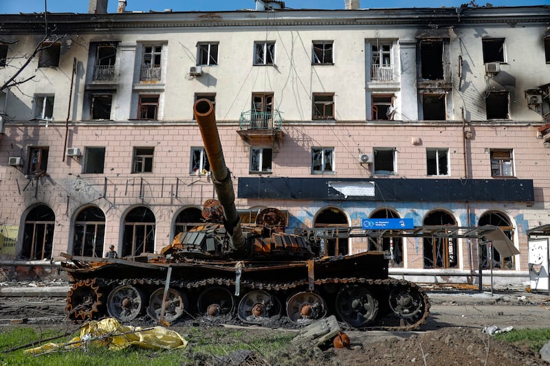 A destroyed tank and a damaged apartment building in Mariupol. AP