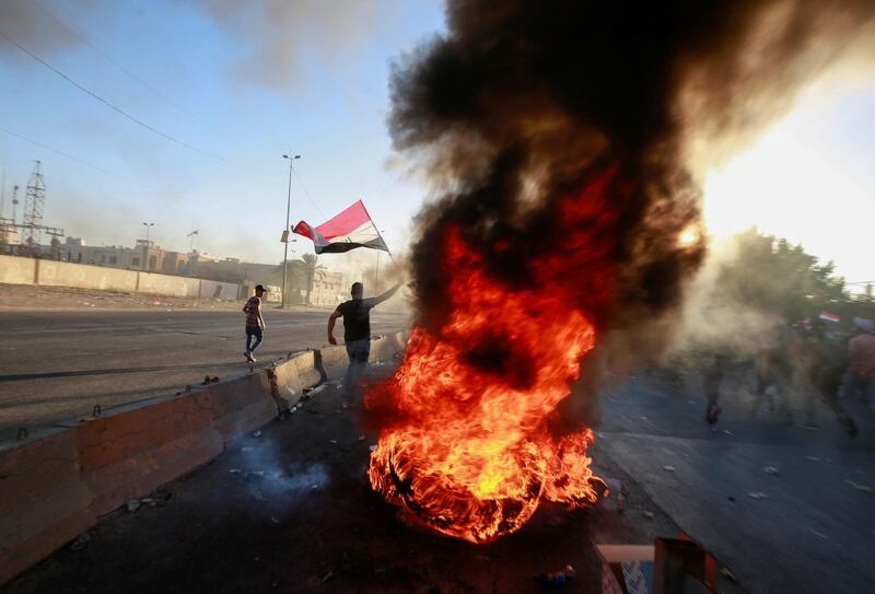 A demonstrator holds the Iraqi flag near burning objects at a protest during a curfew, three days after the nationwide anti-government protests turned violent, in Baghdad, Iraq. Reuters