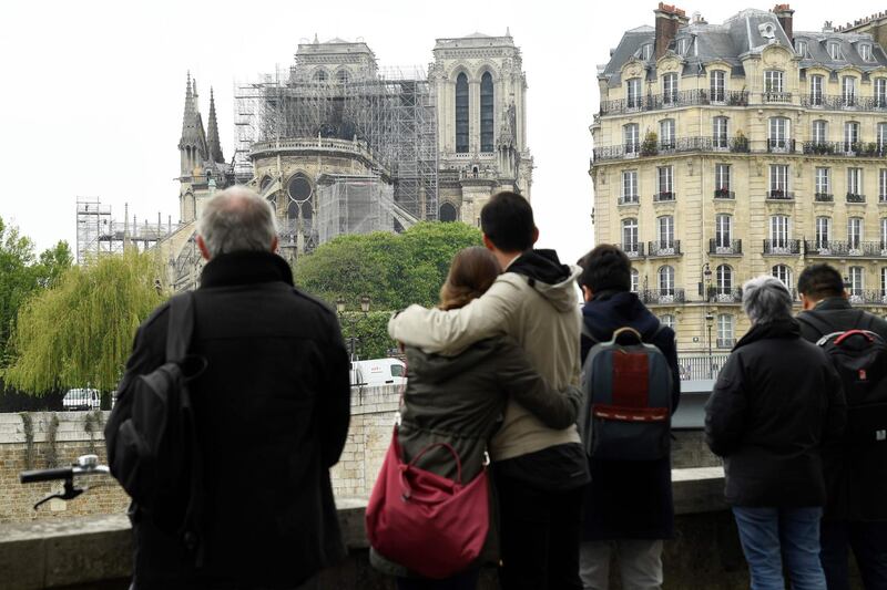 TOPSHOT - People hug while looking at Notre-Dame-de-Paris on April 16, 2019 in the aftermath of a fire that devastated the cathedral.
 Paris was struck in its very heart as flames devoured the roof of Notre-Dame, the medieval cathedral made famous by Victor Hugo, its two massive towers flanked with gargoyles instantly recognisable even by people who have never visited the city. / AFP / Bertrand GUAY
