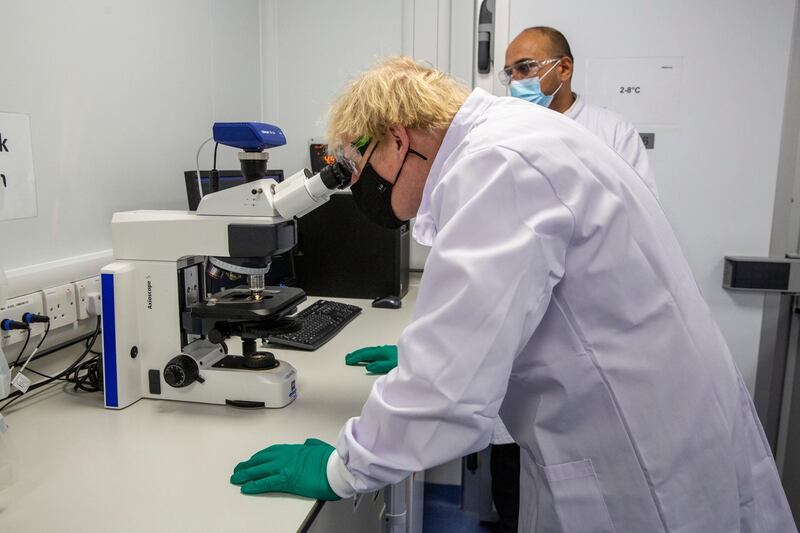 Boris Johnson looks at a vaccine sample through a microscope. Getty Images