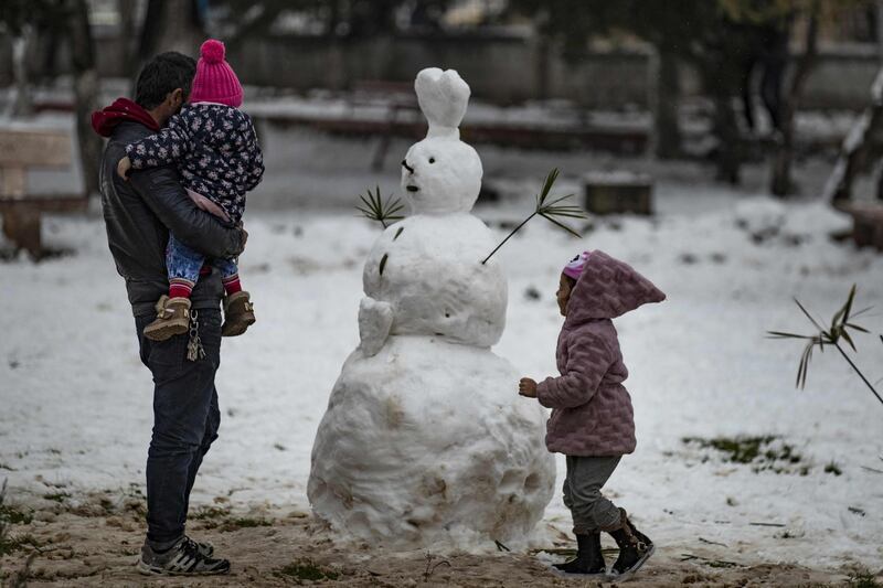 A man stands with his child near a snowman in the de-facto Syrian Kurdish capital of Qamishli. AFP