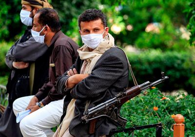 TOPSHOT - A fighter loyal to Yemen's Huthi rebels acting as security, looks on while wearing a face mask and latex gloves and slinging a Kalashnikov assault rifle as volunteers part of a community-led initiative to prevent the spread of COVID-19 coronavirus disease gather in Yemen's capital Sanaa on May 14, 2020.  / AFP / MOHAMMED HUWAIS
