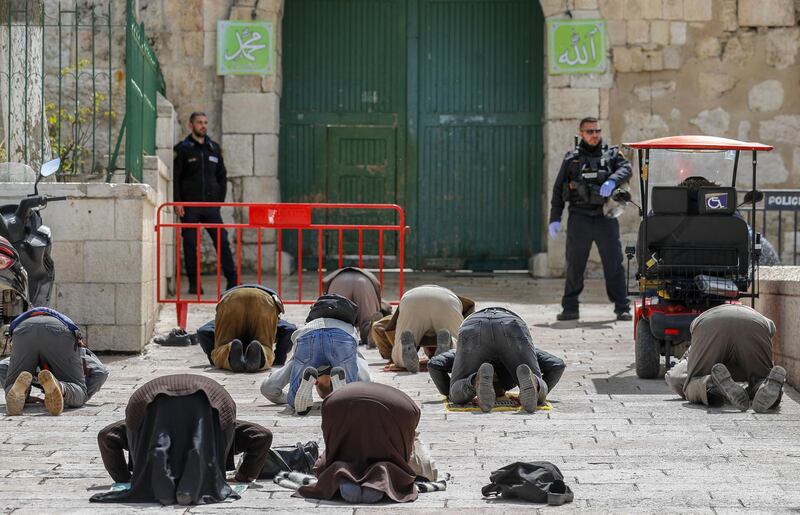 This picture taken on March 23, 2020 shows Palestinian Muslim men prostrate in prayer as Israeli security forces watch near the closed gate of the Aqsa mosque compound, which was closed by the Jordan Waqf religious authority administering the site as part of preventive measures against the spread of the COVID-19 novel coronavirus, in Jerusalem.  / AFP / Ahmad GHARABLI

