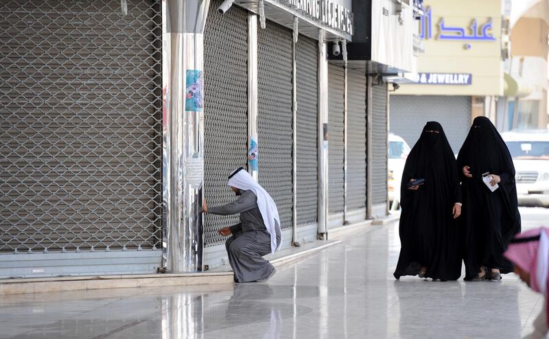 Saudi women walk past a jeweller arriving to open his shop in the Tiba gold market in the capital Riyadh on February 27, 2018. - The Riyadh gold souk is short of salesmen after a government edict to replace foreign workers with Saudis as part of contentious efforts to tackle high unemployment, with many of them who have been long accustomed to a generous cradle-to-grave welfare system regard such jobs as degrading. (Photo by Fayez Nureldine / AFP)