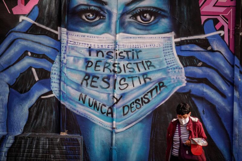 A woman walks in front of a mural that reads "insist, persist, resist and never give up" in Bogota, Colombia. Getty Images