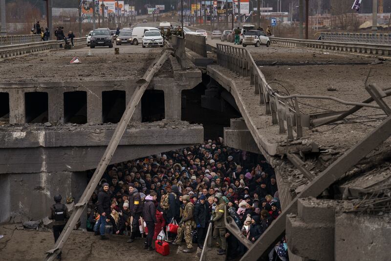 Ukrainians under a destroyed bridge as they as they cross the Irpin river on the outskirts of Kyiv in March 2022