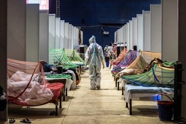 A medical worker in PPE observes patients who have been infected by Covid-19 inside a makeshift covid care facility in a sports stadium at the Commonwealth Games Village in New Delhi. Getty