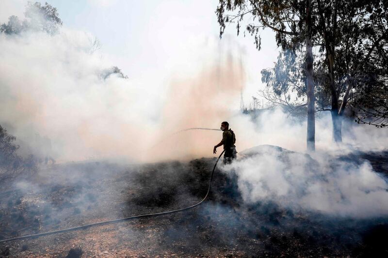 An Israeli soldier attempts to extinguish a fire in a forest field near the Kibbutz of Nahal Oz, along the border with the Gaza Strip, on July 17 after it was caused by inflammable material attached to a balloon flown by Palestinian protesters from across the border.  / AFP / MENAHEM KAHANA
