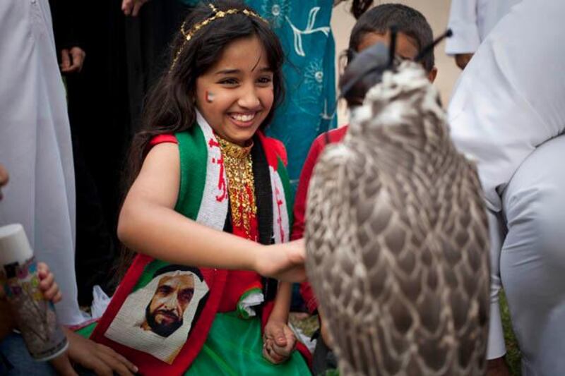 Abu Dhabi, United Arab Emirates - December 02 2012- A young local girl smiles as she touches a falcon at Heritage Village along the breakwater for the celebration of the UAE's 41st National Day. (Razan Alzayani / The National)